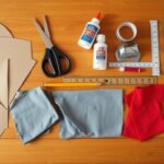 Materiały potrzebne do zrobienia stroju rycerza samemu, rozłożone na stole: karton, nożyczki, klej, farby, tkaniny